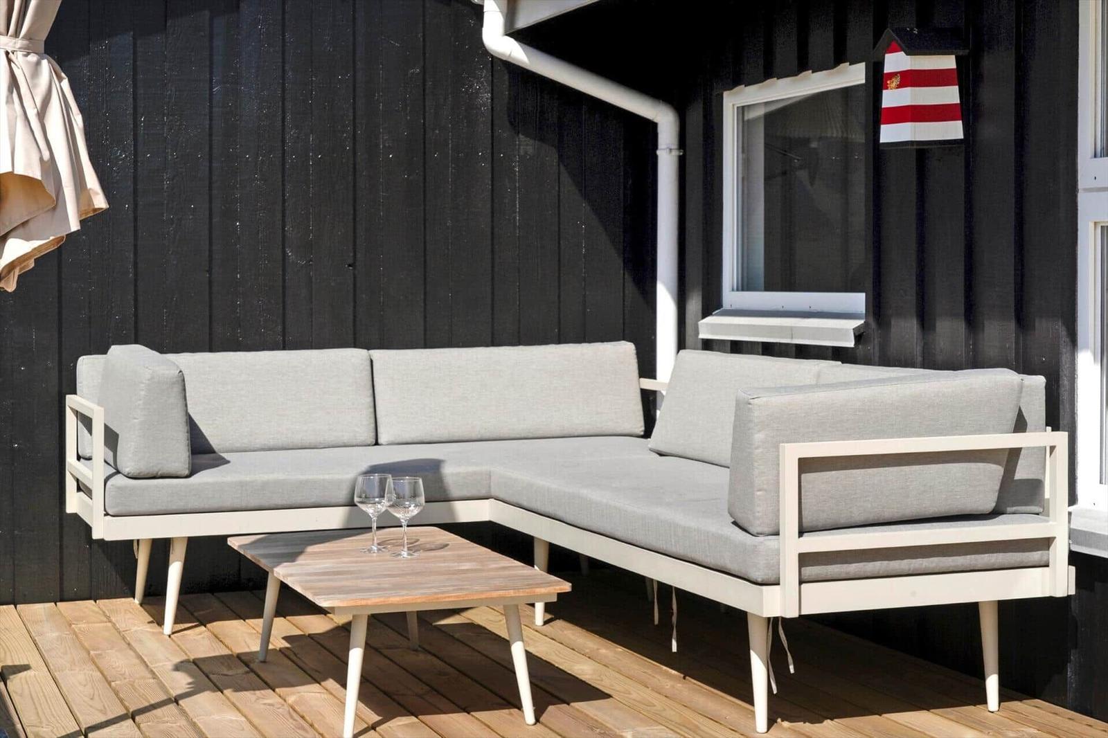 Terrasse mit grauem Ecksofa und Holztisch. Hintergrund: schwarze Wand und Fenster.