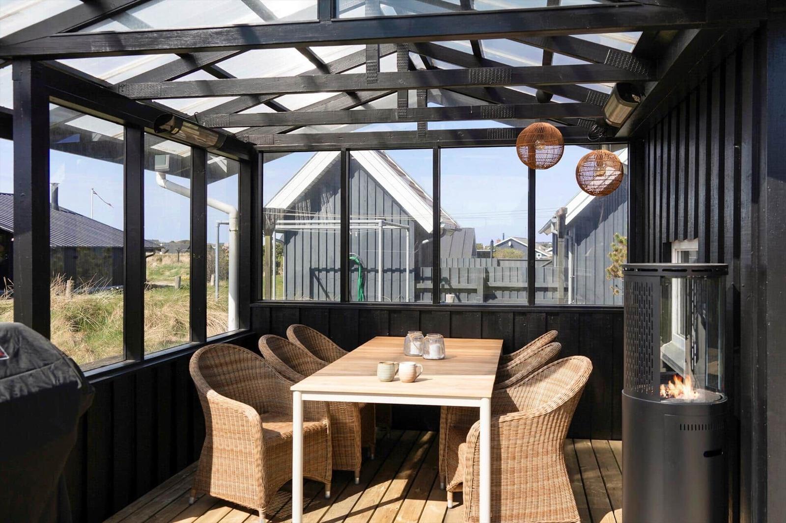 Terrasse mit Tisch, Stühlen und Feuerkamin. Glasdach und Sicht auf Umgebung.