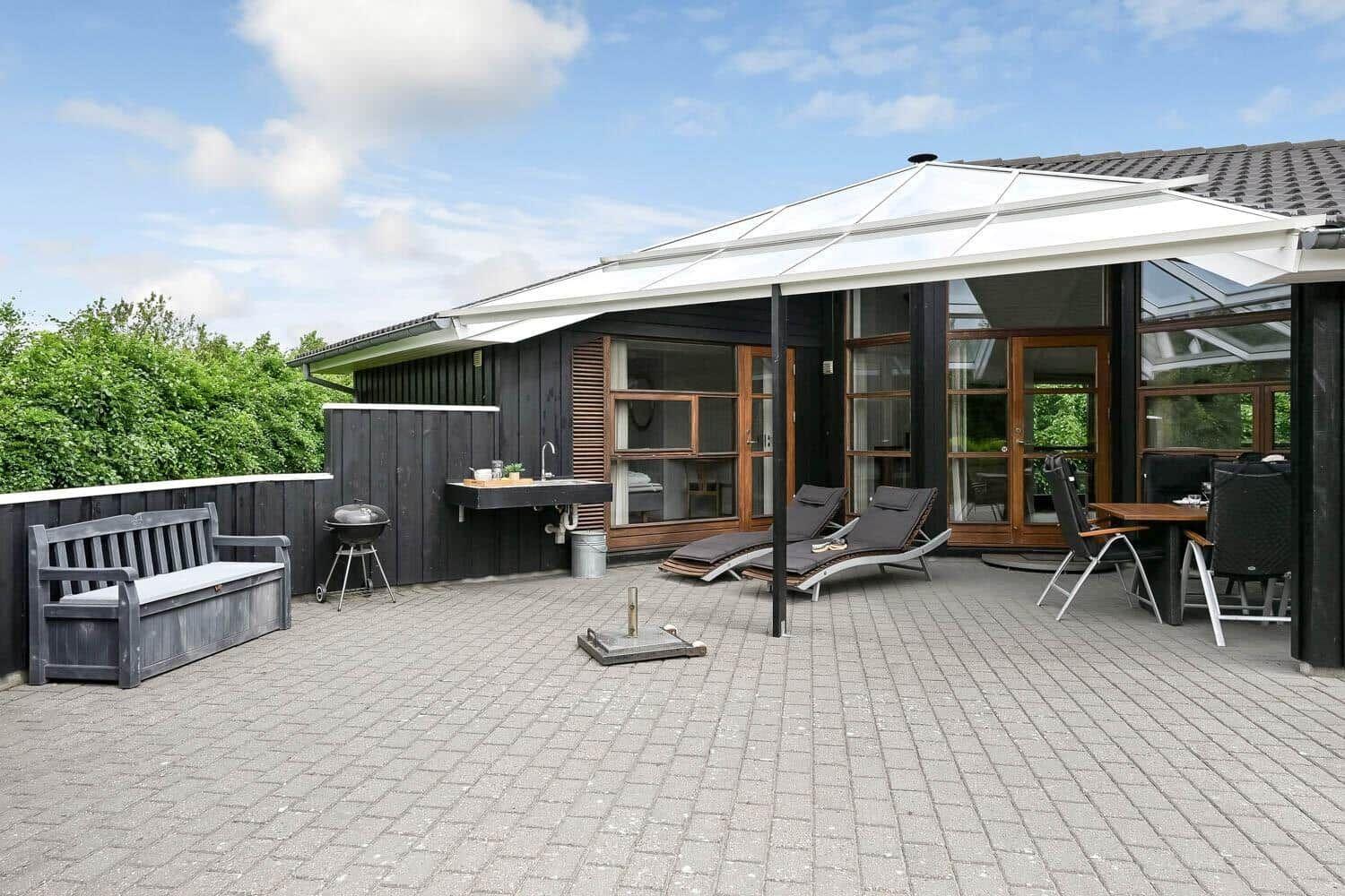 Terrasse mit Liegen, Grill und Sitzbank vor modernem Haus mit Glasfront.