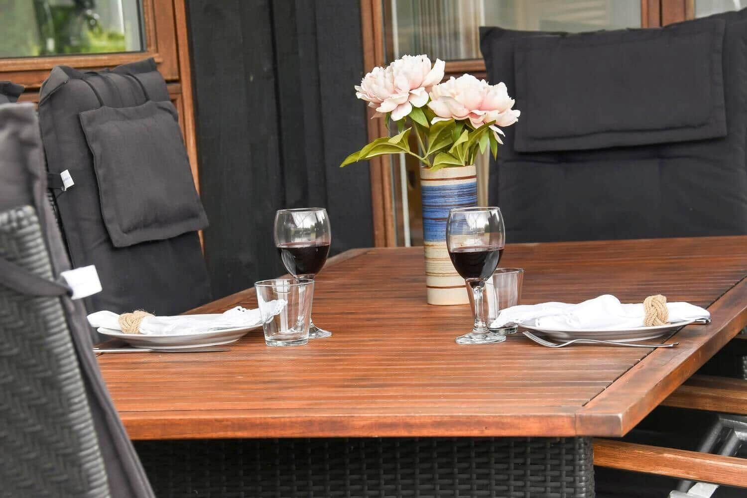Holztisch mit zwei Platzsetzungen, Wein und Blumen auf der Terrasse.
