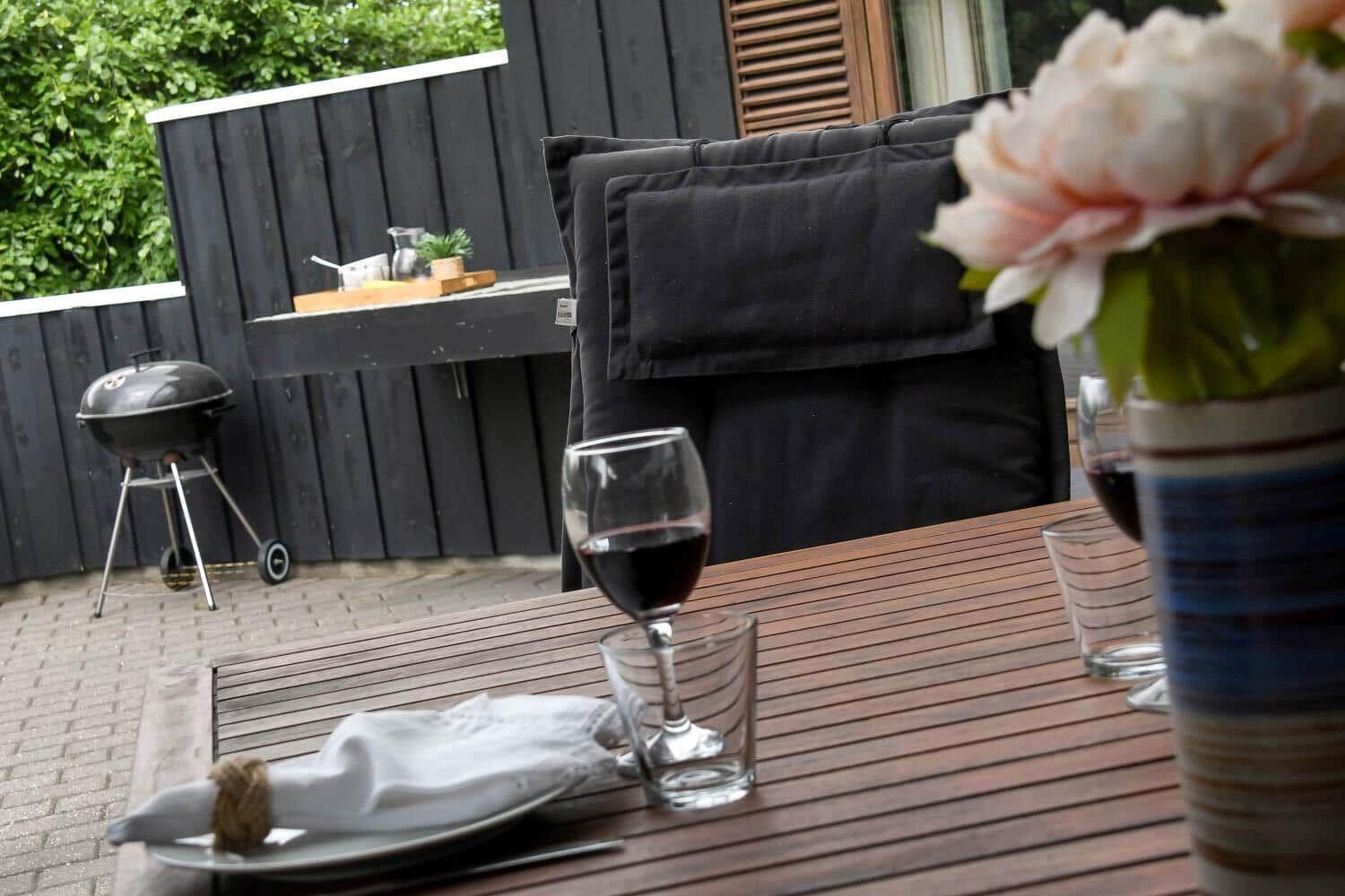 Außenbereich mit Tisch, Stühlen, Grill und Blumenvase.