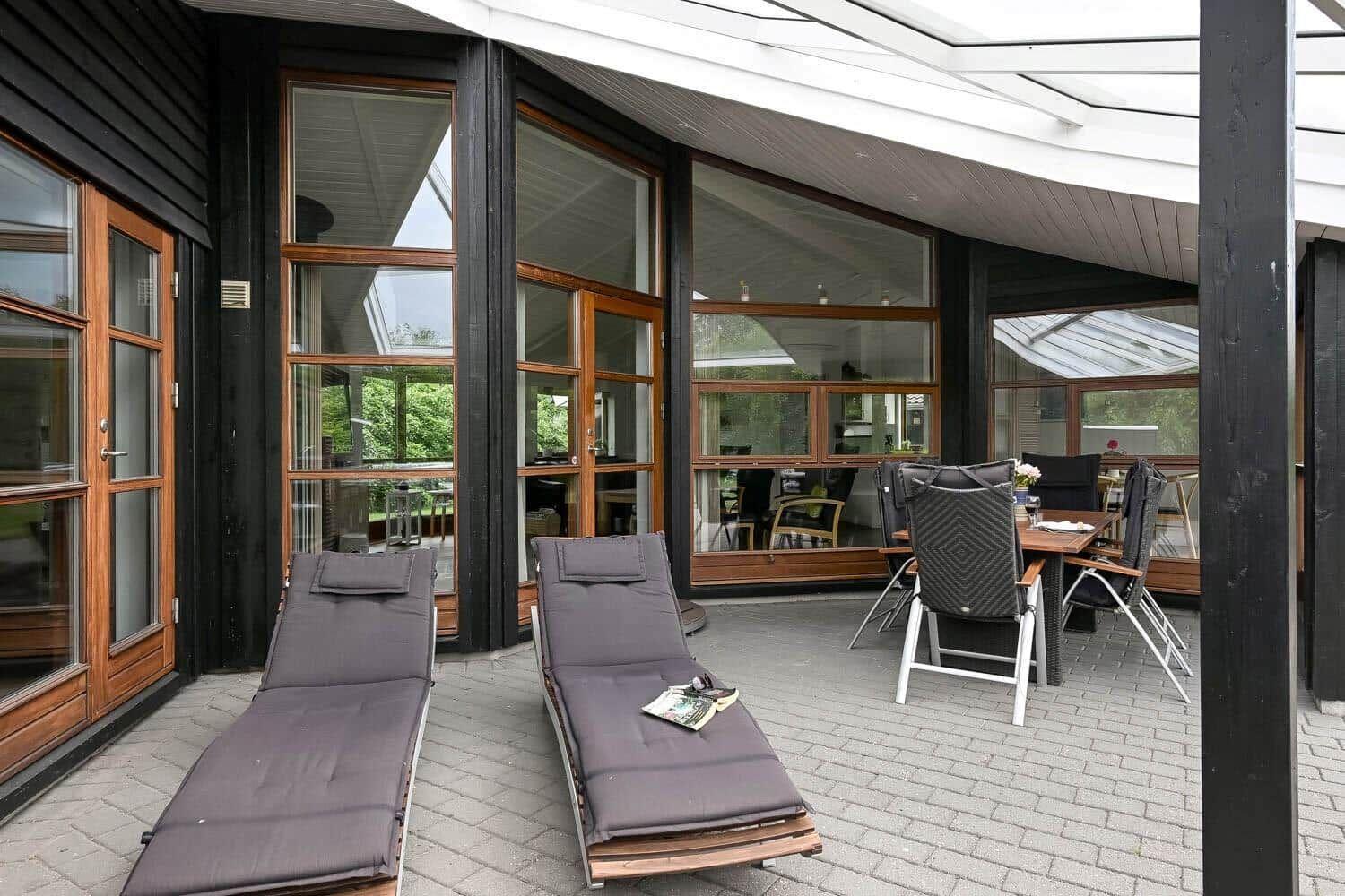 Terrasse mit Liegen und Tisch. Durchgehende Glaswände. Holzrahmen. Dachkonstruktion.