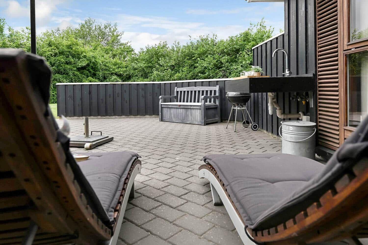 Terrasse mit Liegestühlen, Grill und Waschbecken an der Wand.