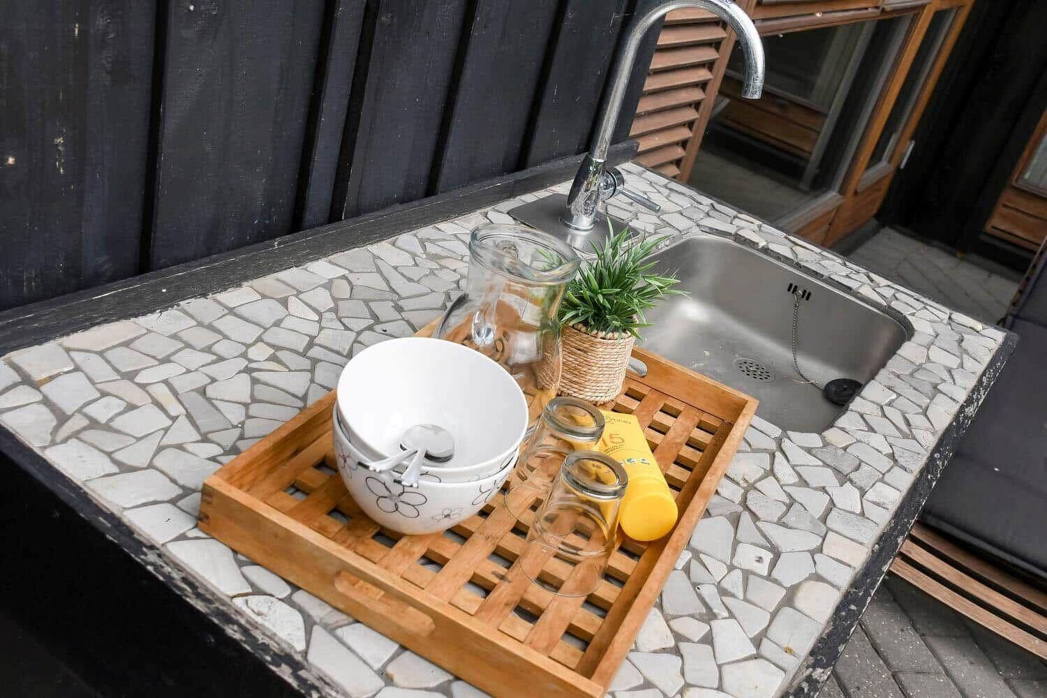 Außenbereich mit Waschbecken, Mosaikarbeitsplatte und Holztablett mit Geschirr.