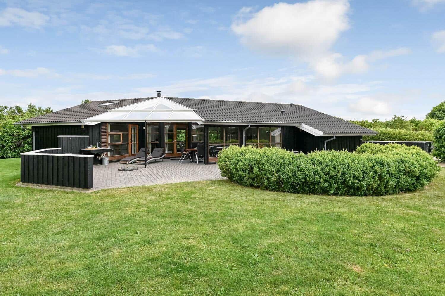 Moderne Villa mit großem Garten und Terrasse mit Sonnenschirm und Liegestühlen.