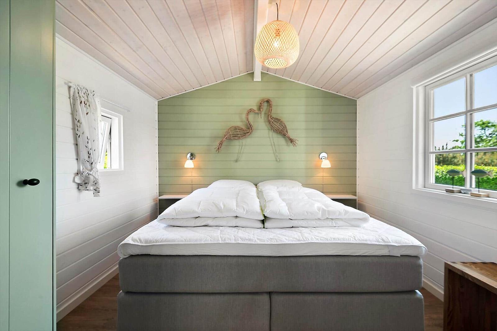 Schlafzimmer mit Bett, Fenstern und Deckenleuchte.