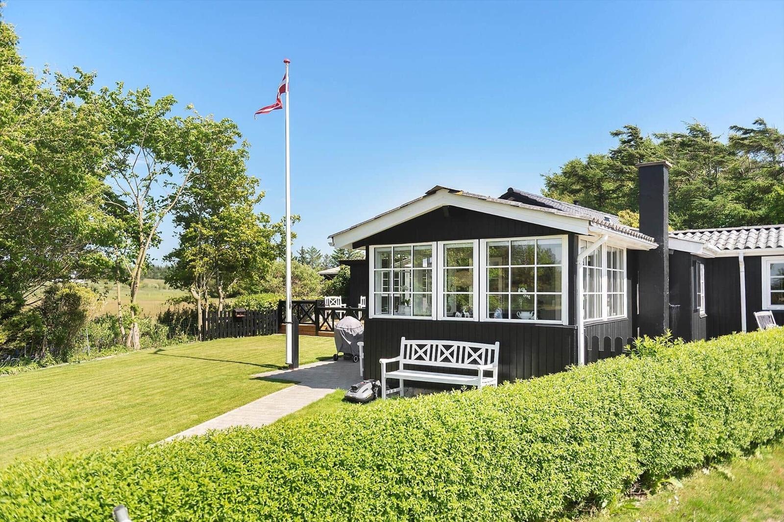 Schwarzes Holzhaus mit weißem Fensterrahmen, Garten und Flagge.