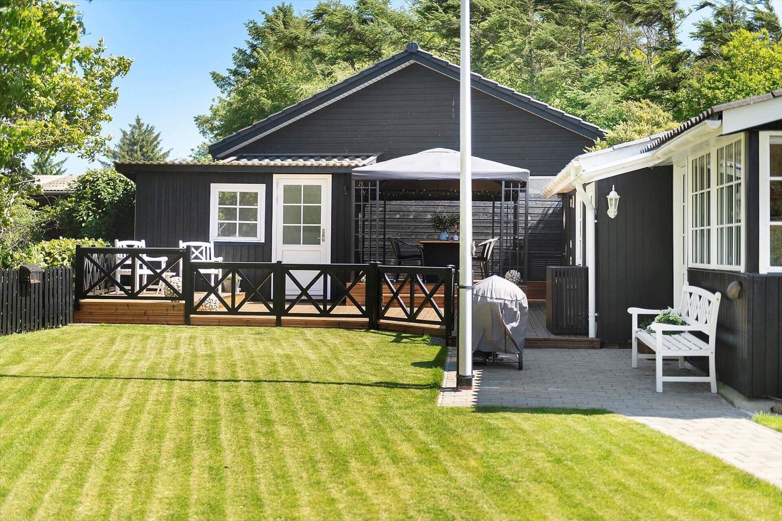 Schwarzes Ferienhaus mit Terrasse, Garten und weißen Möbeln.