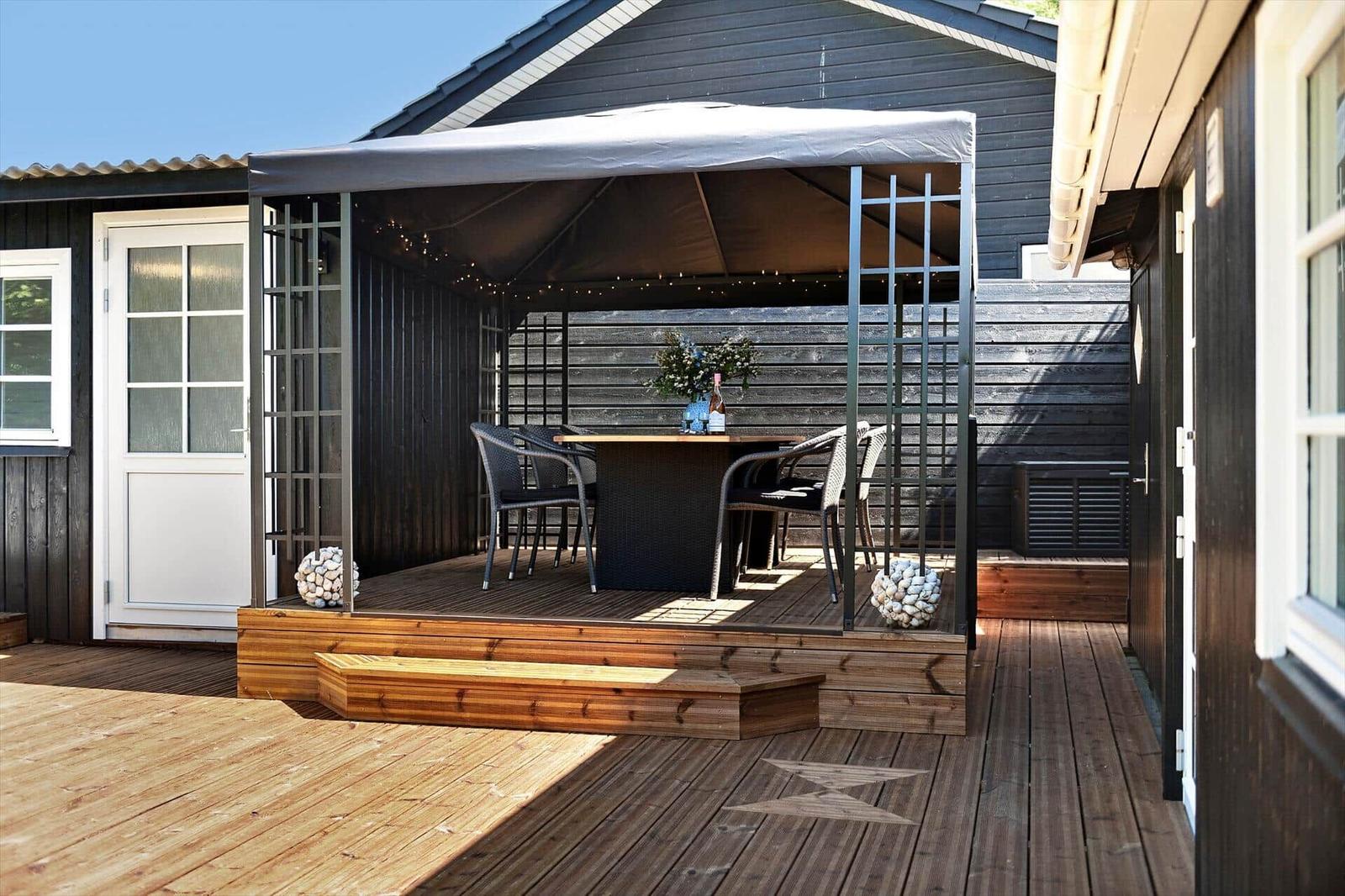 Terrasse mit Pavillon, Tisch und Stühlen. Holzdecke und schwarze Wandverkleidung.
