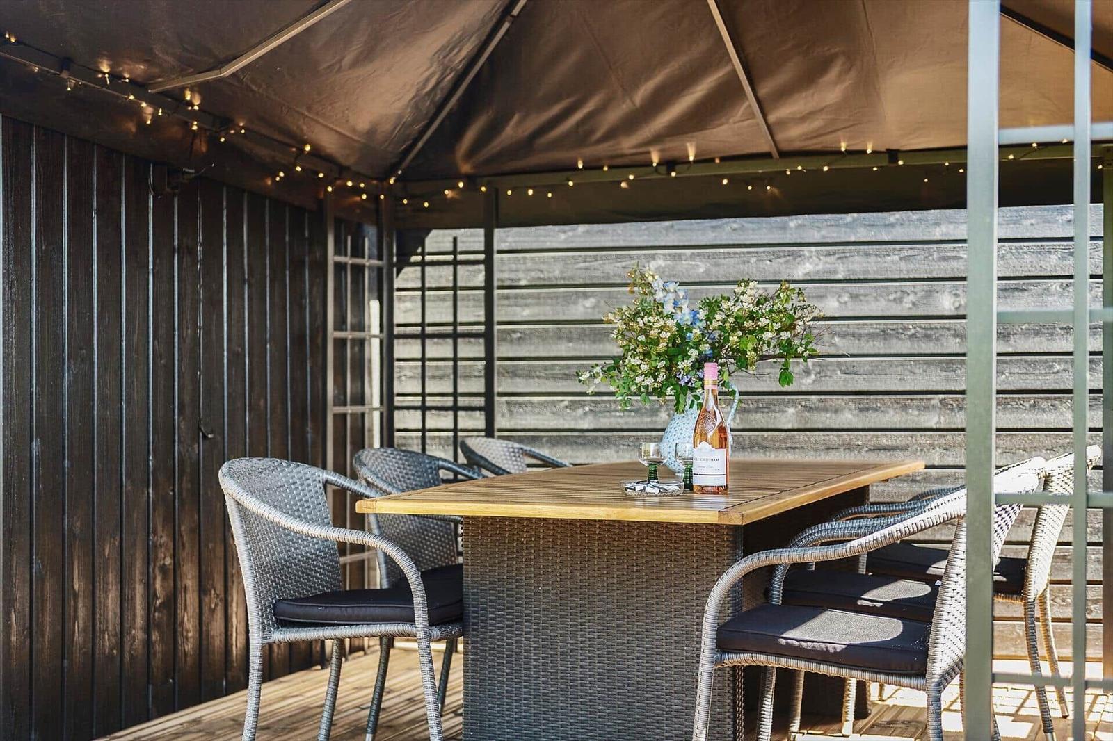 Terrasse mit Tisch, Stühlen und Blumenarrangement unter Markise.