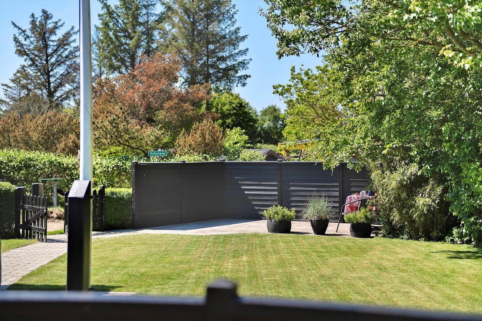 Garten mit Rasen, Pflanzen und Terrasse hinter dunklem Zaun