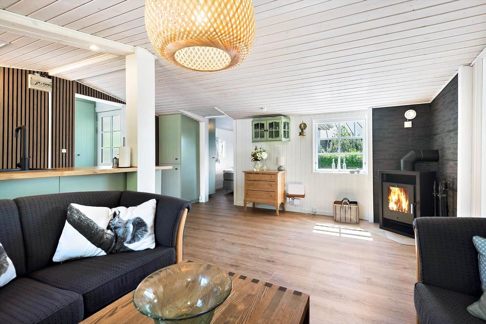 Wohnzimmer mit Kamin, Sofa und Holzboden. Küche und Schlafzimmer sind sichtbar.
