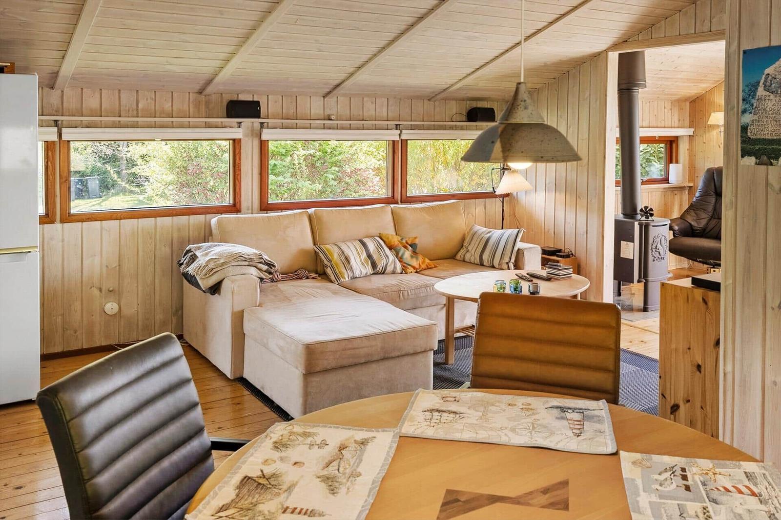 Living room with sofa, dining table, and wood walls. Doorways to kitchen and fireplace room.