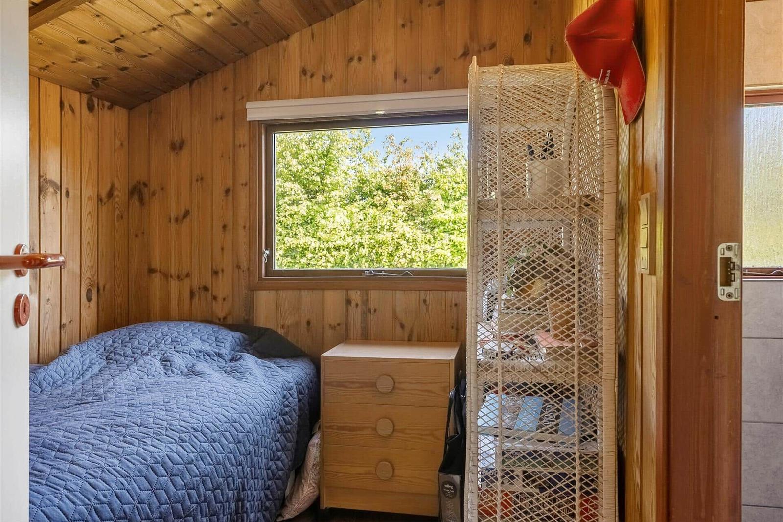 Bedroom with wooden walls, bed, and window with view of trees.