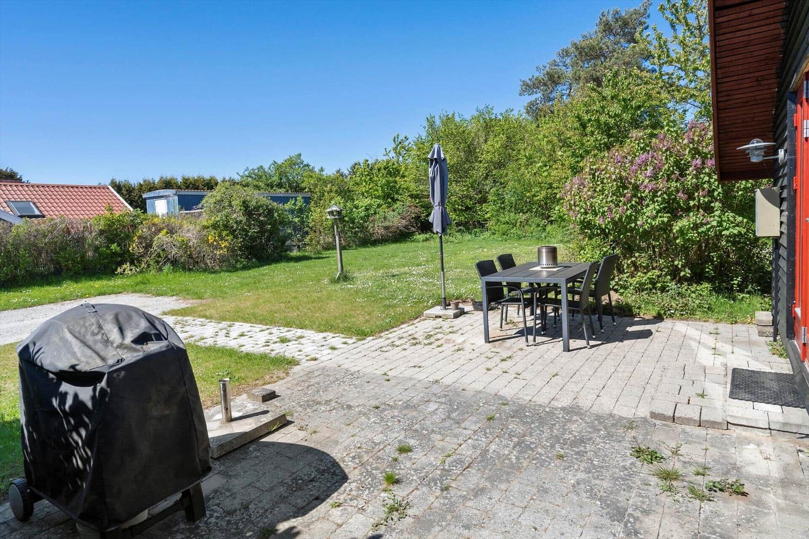 Terrace with table, chairs, and covered grill. Background: lawn and trees.