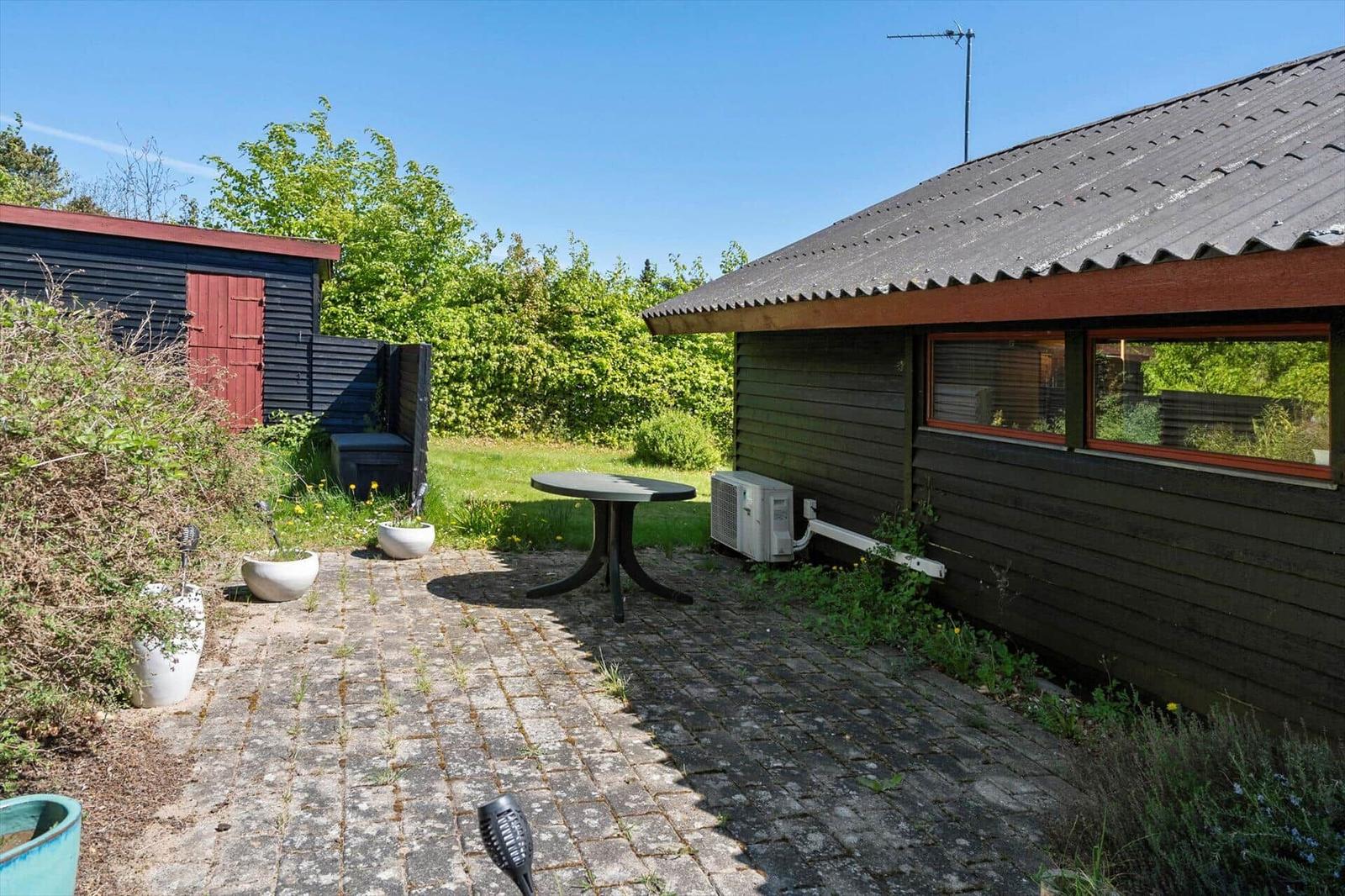 Outdoor area with table, plants, and wooden house under blue sky.