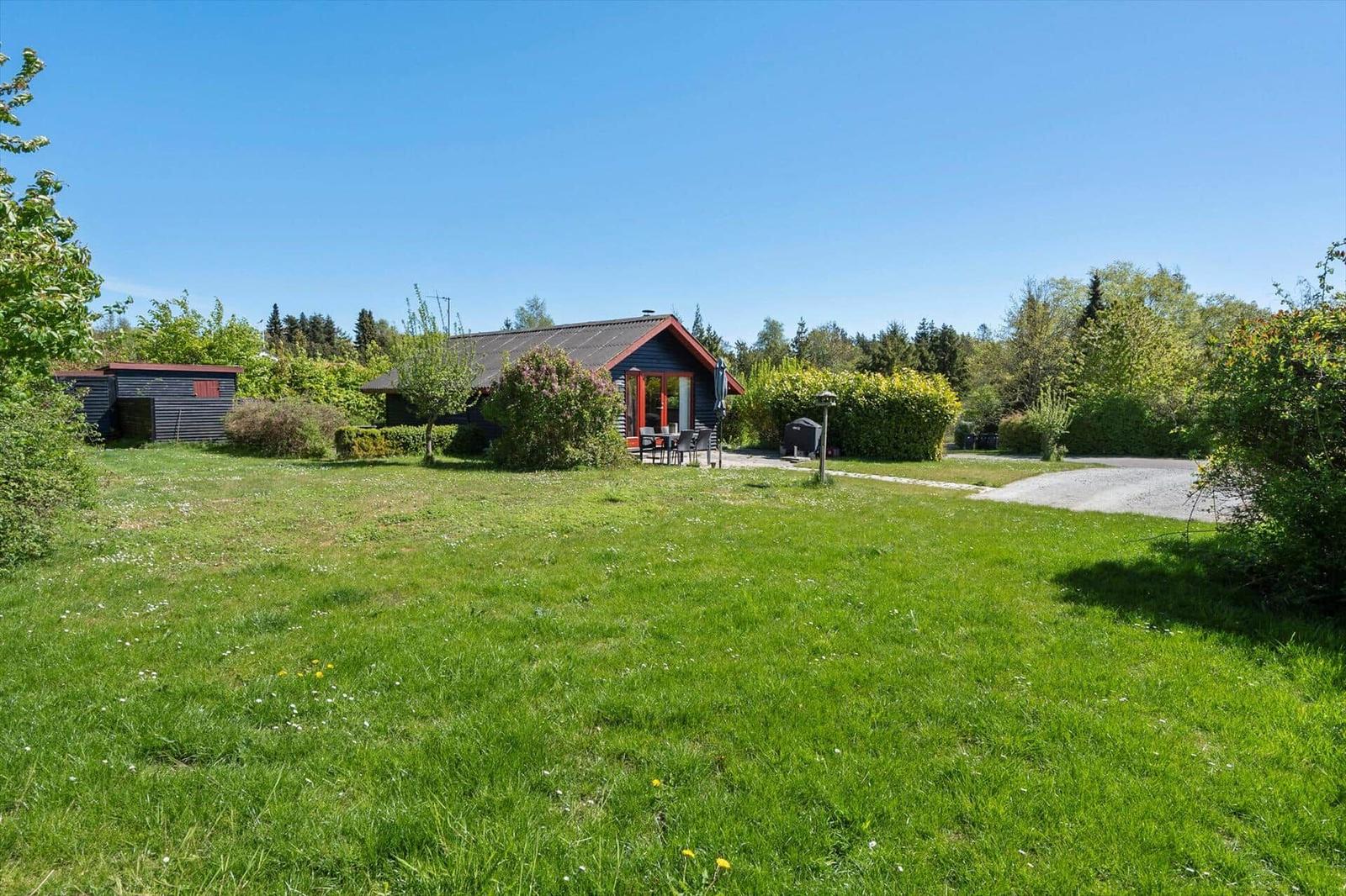 A small house with red entrance and garden. Lawn, trees, and clear sky.