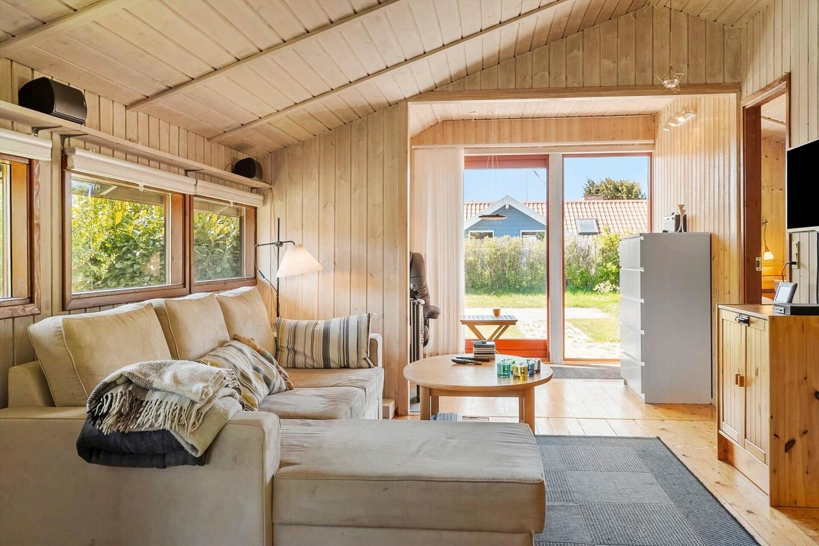 Living room with sofa, coffee table, and wood paneling. Doorway to terrace with garden view.