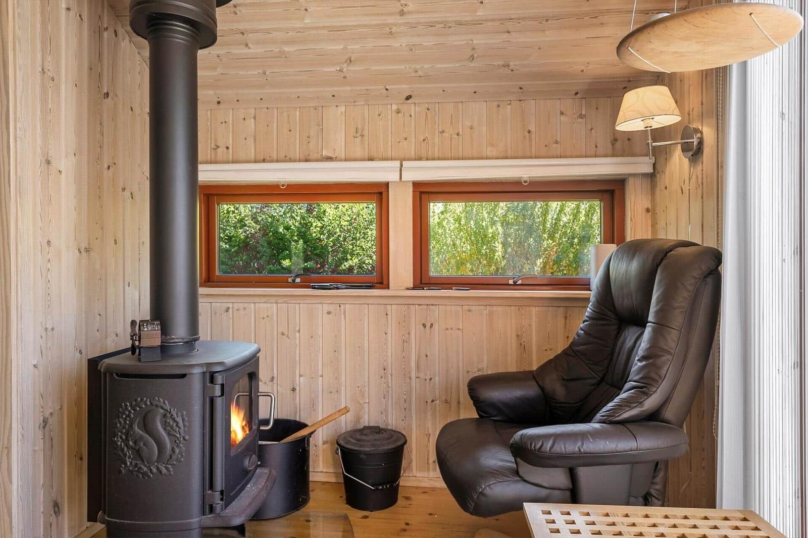 Room with wooden walls, wood stove, and leather recliner by windows with green view.