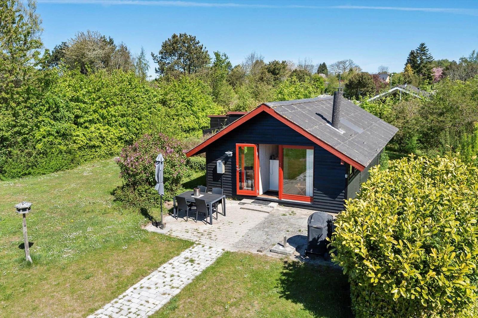 Modern wooden cabin with garden, terrace, and grill area. Surrounded by greenery and trees.