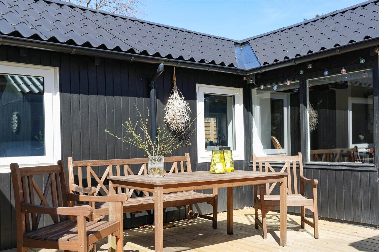 Holzterrasse mit Tisch und Stühlen vor schwarzem Haus mit Dach und Fenstern.