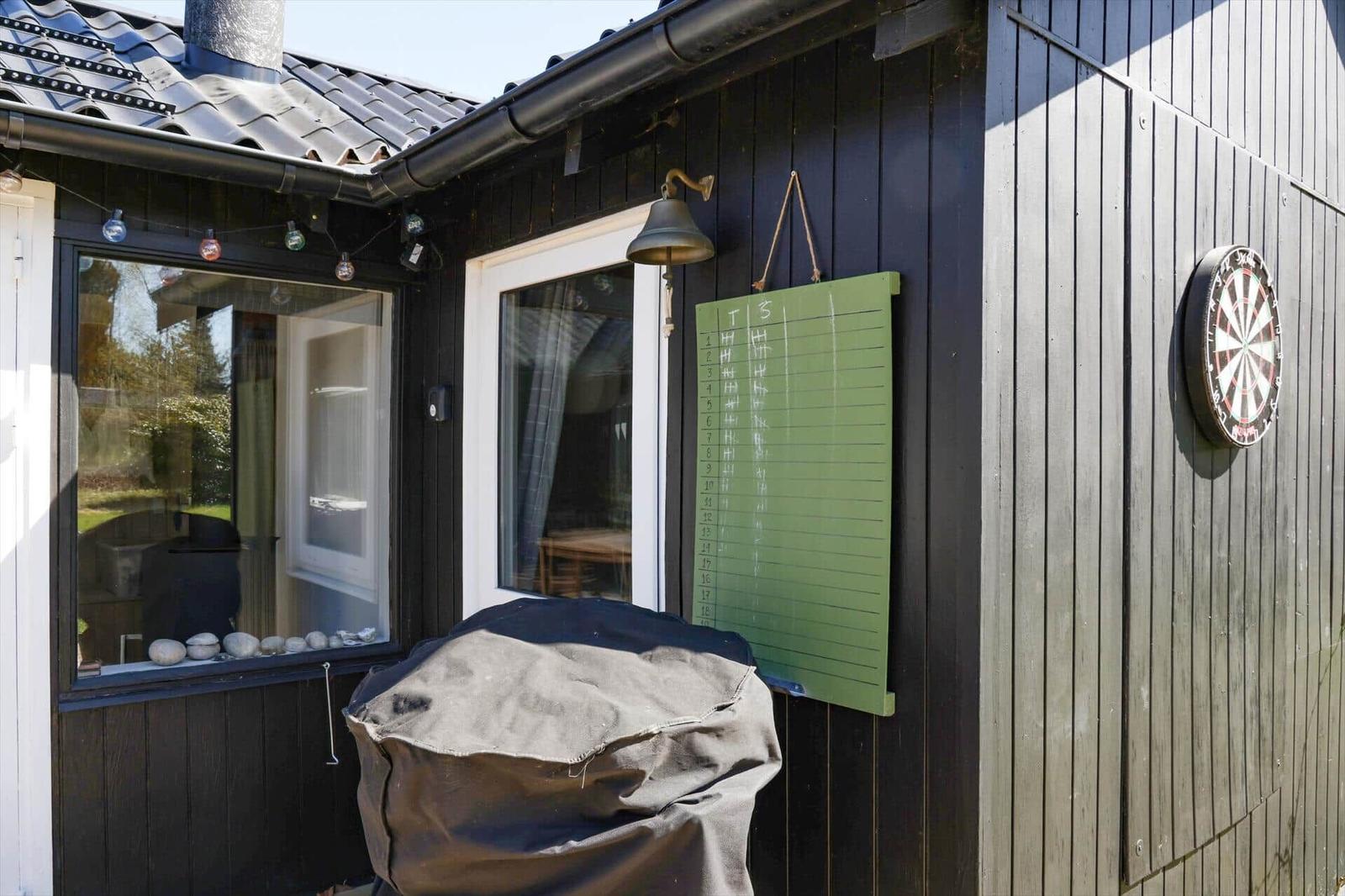 Außenbereich mit Dartboard, grünem Tafel und Grilldecke an schwarzem Holzhaus.