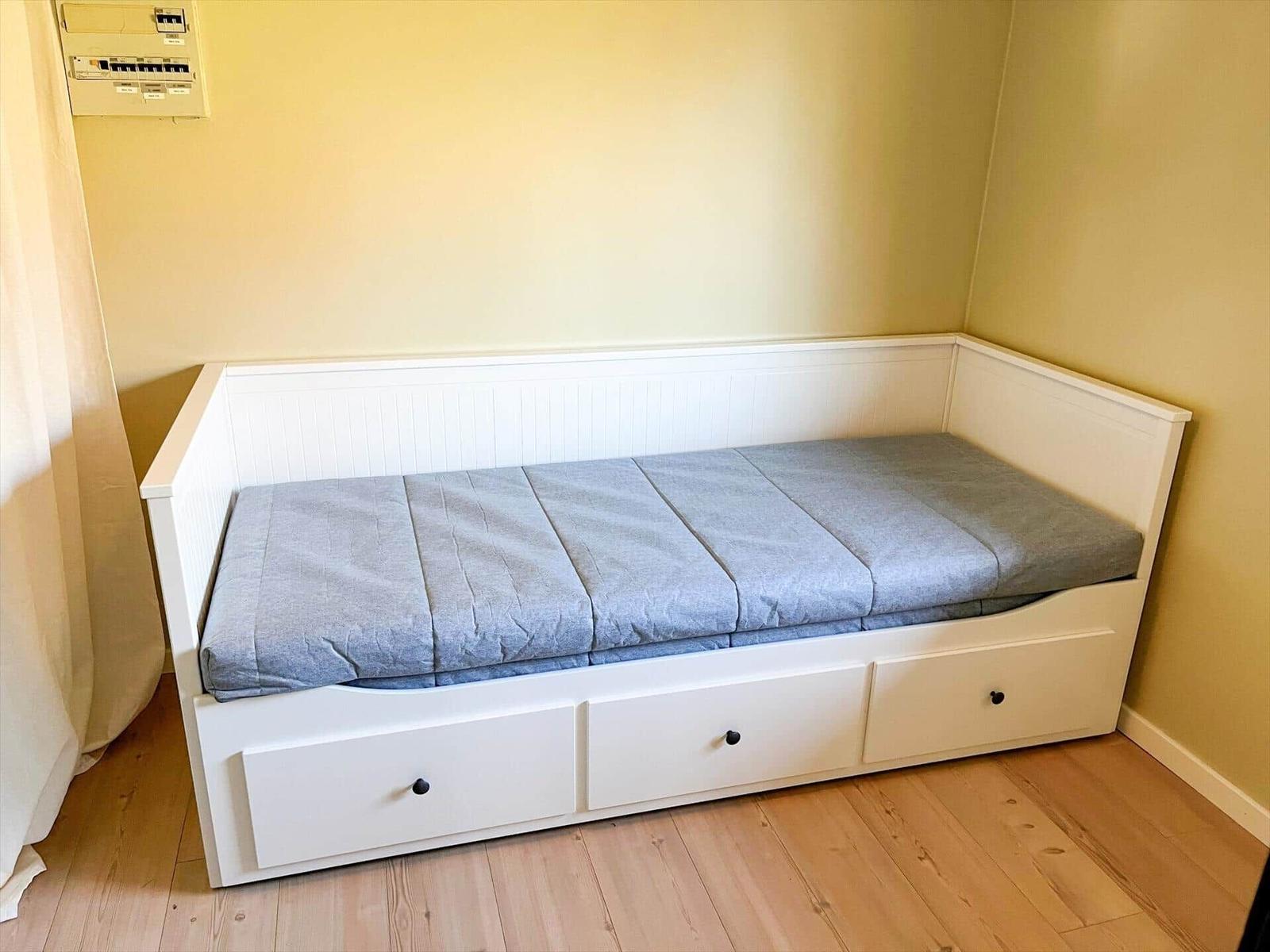Ein weißes Bett mit drei Schubladen und einem grauen Matratzenbezug.