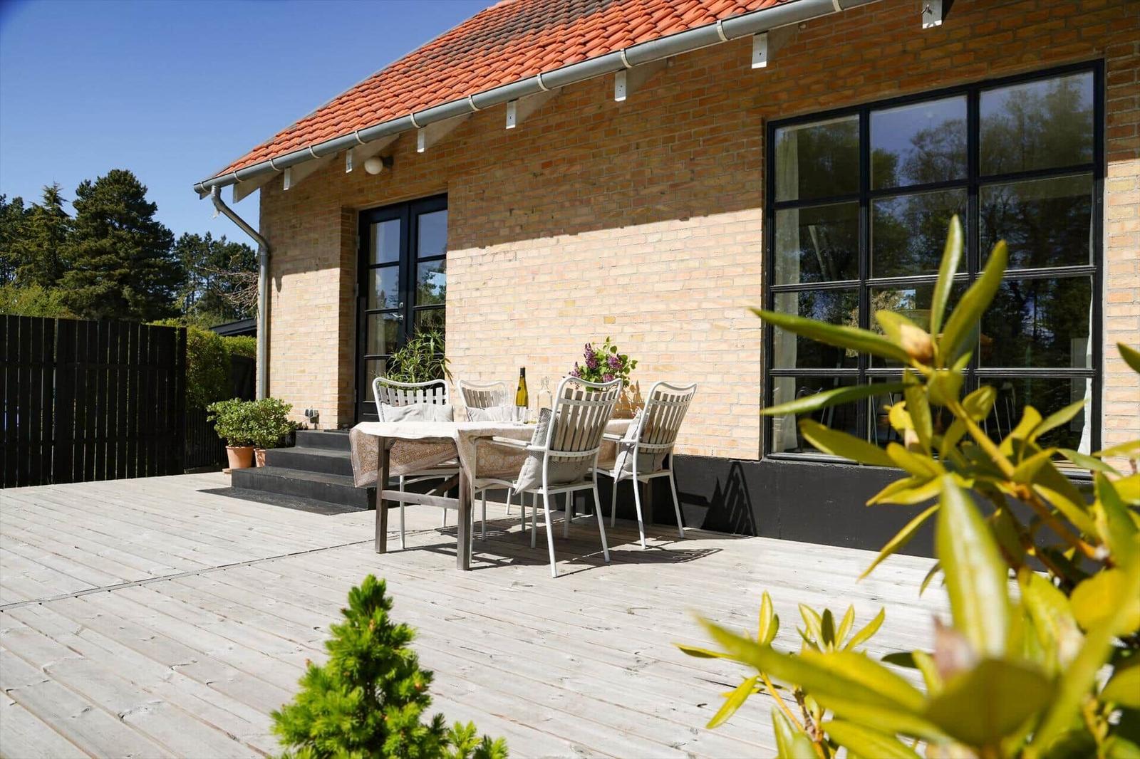 Deck with table and chairs in front of a brick house with red roof.