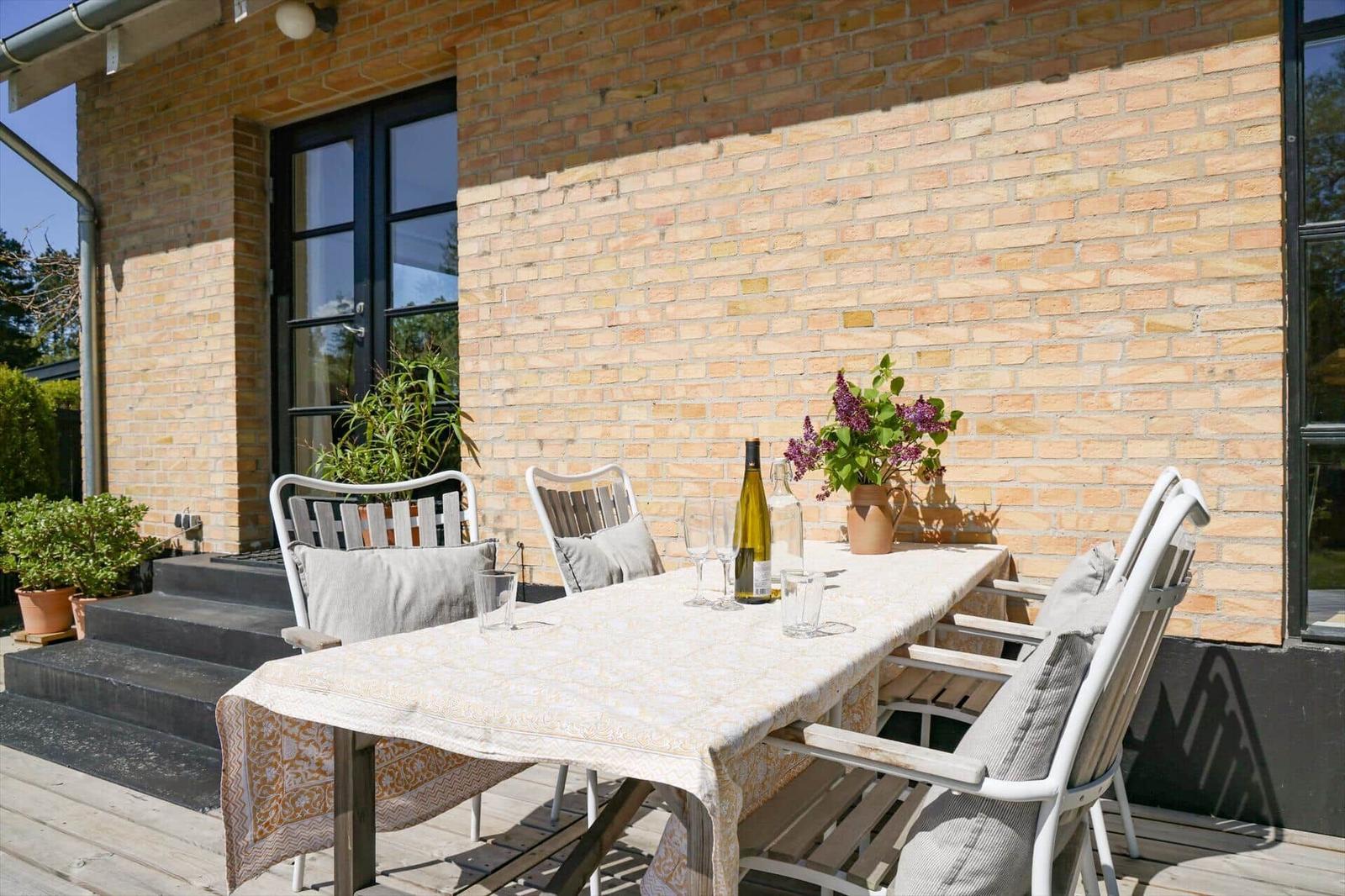 Terrace with table, chairs, flowers, and wine bottle against brick wall.