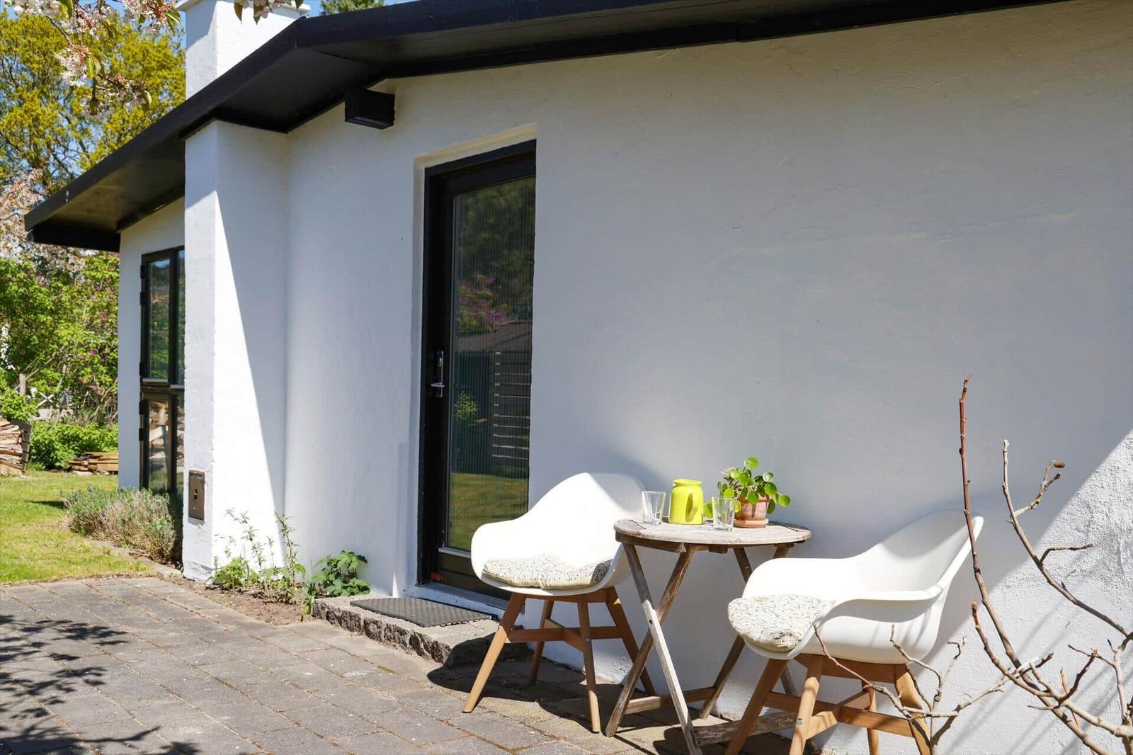 House with terrace, two white chairs and table with plant.