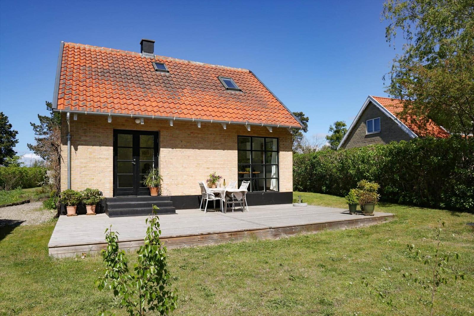 A house with terrace, garden, and red roof under blue sky.