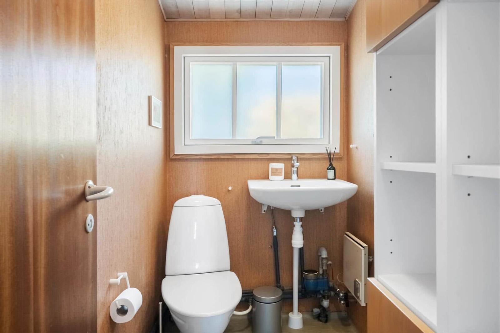 Badezimmer mit Toilette, Waschbecken und Fenster. Holzwände und weißer Einbau.