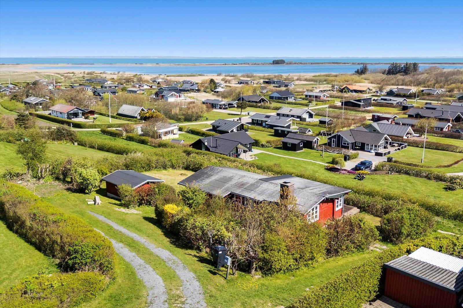 Rotes Ferienhaus mit Garten, umgeben von Grünflächen und Blick aufs Wasser.