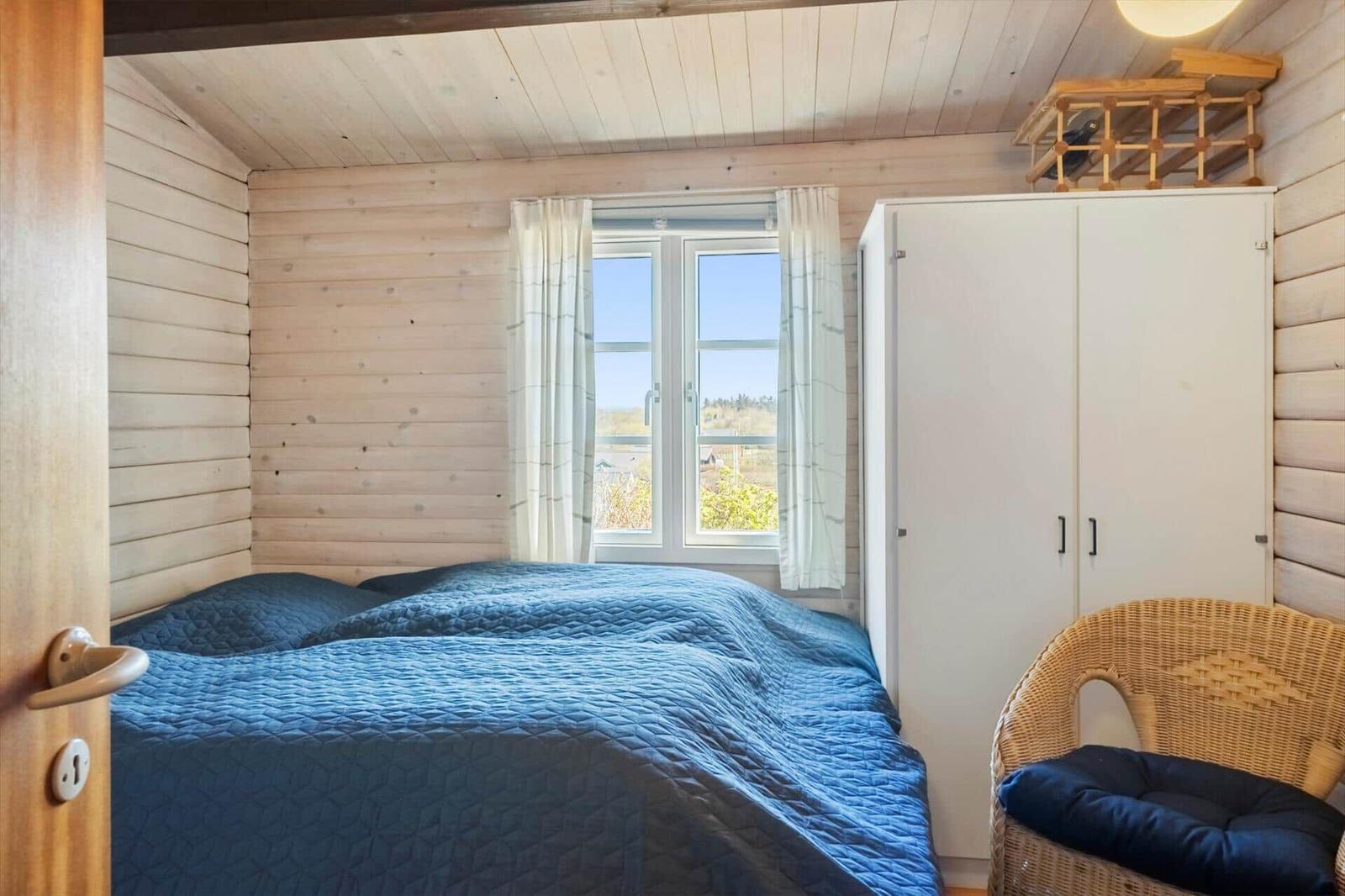 Schlafzimmer mit Holzwand, Bett, Fenster und Schrank.