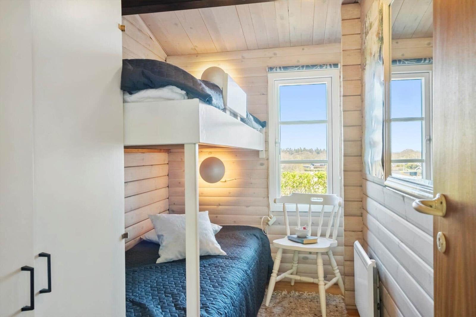 Schlafzimmer mit Doppelstockbett, Fenster und Stuhl.