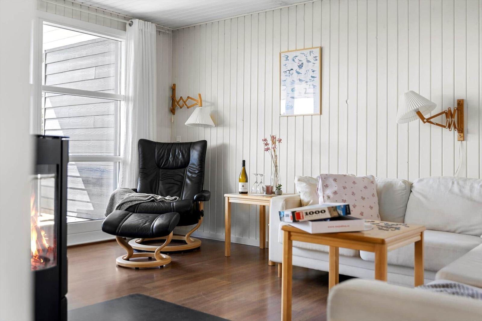 Wohnzimmer mit Sofa, Sessel, Tisch und Kamin. Wandbeleuchtung und Fenster sichtbar.