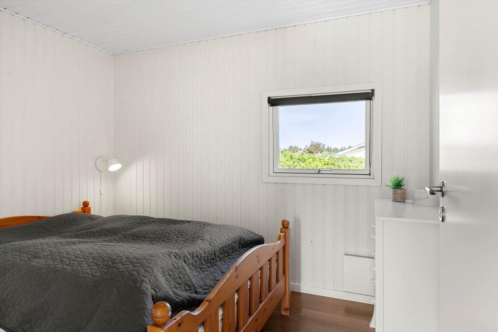 Schlafzimmer mit Holzbett, Fenster und Schrank. Wandverkleidung und Boden aus Holz.