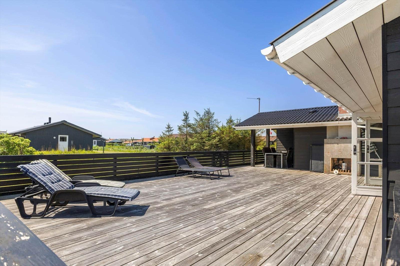 Terrasse mit Liegestühlen und Grillbereich. Holzdecke, Sicht auf Grün und Nachbarhaus.