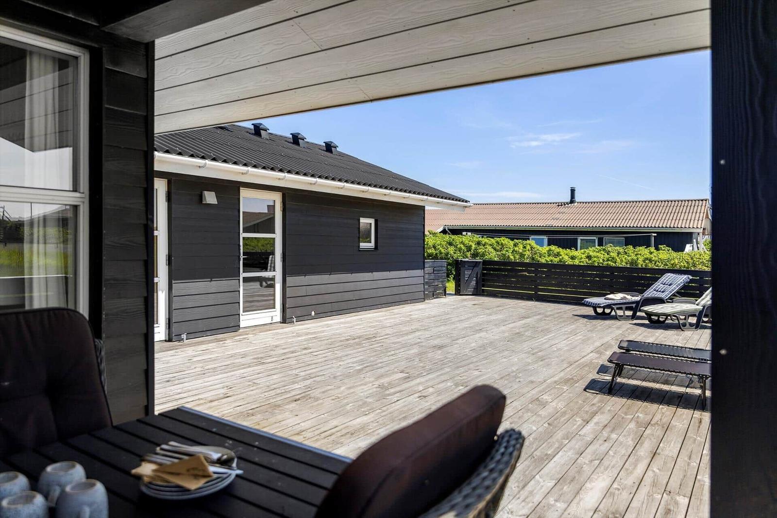 Terrasse mit Liegen und Tisch. Blick auf Haus mit dunkler Fassade.