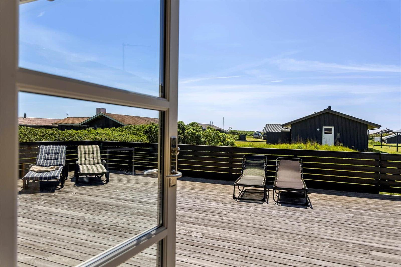Terrasse mit Liegen und Blick auf grüne Landschaft und Gebäude.