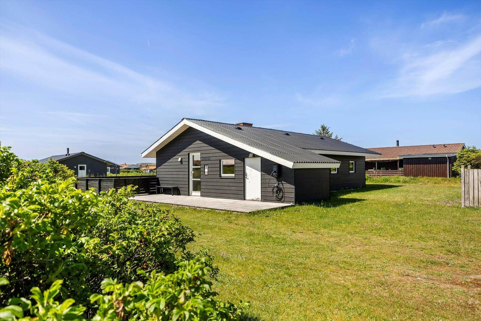 Ein Haus mit grauer Fassade und Holzterrasse auf grünem Grund.