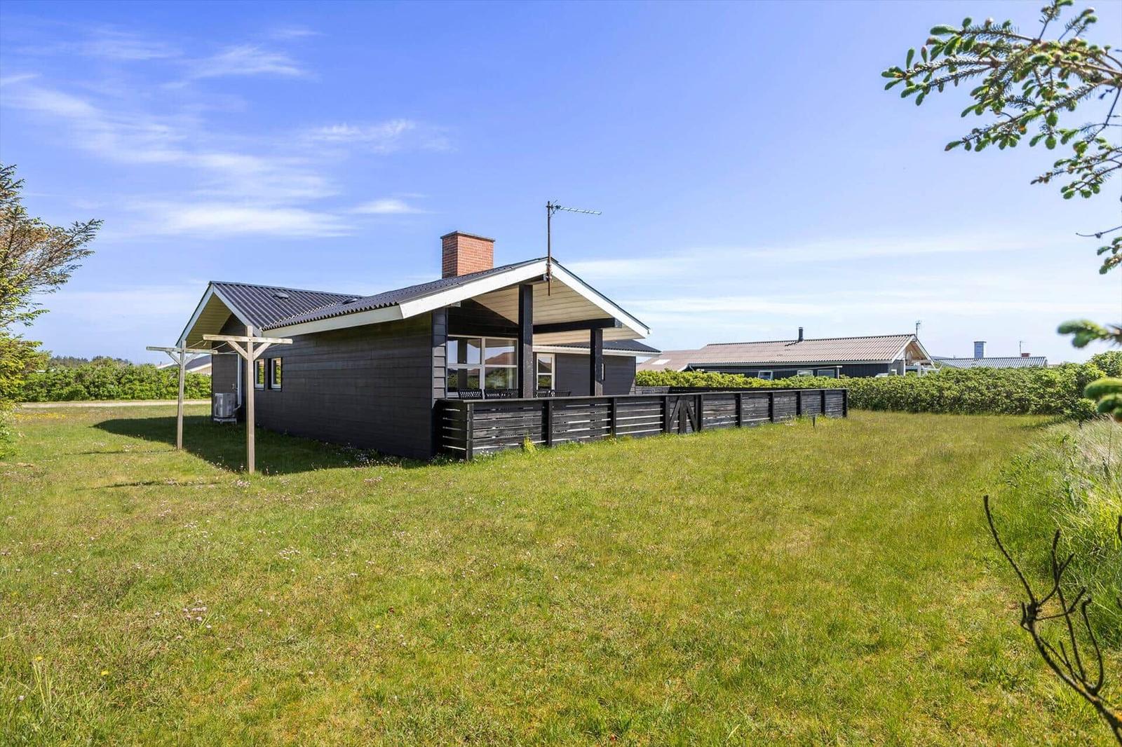 Moderne Villa mit Holzveranda und Garten. Hintergrund: weiteres Haus und Bäume.