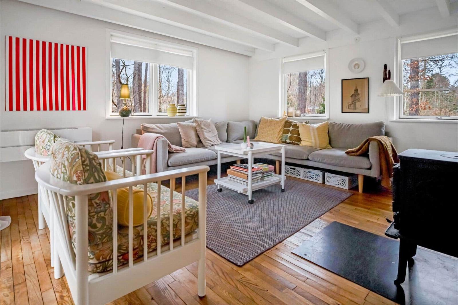 Living room with sofa, chairs, and windows. Wooden floor and wall art.