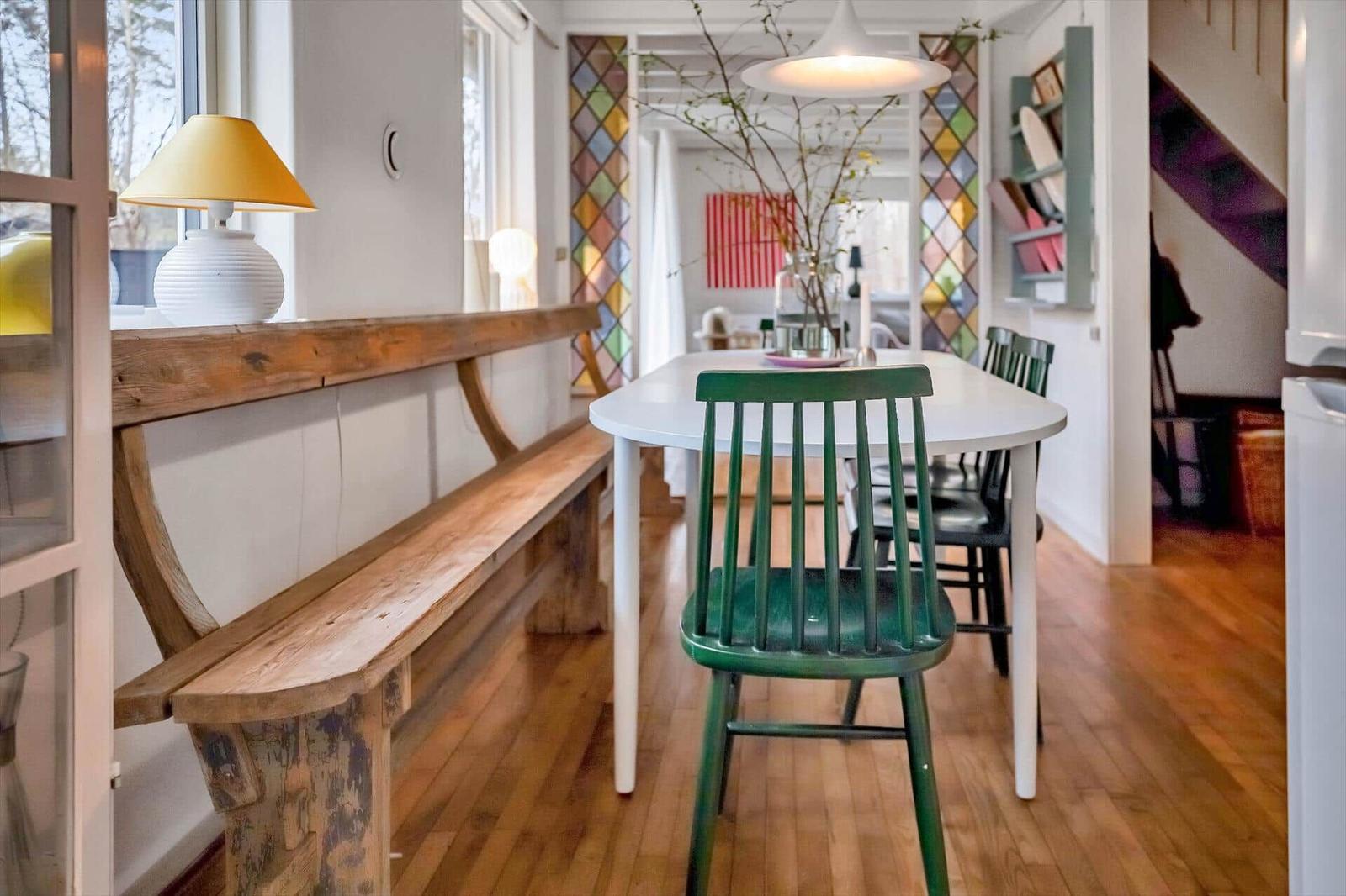 Dining area with green chair and wooden bench. Colorful glass walls and wooden floor.