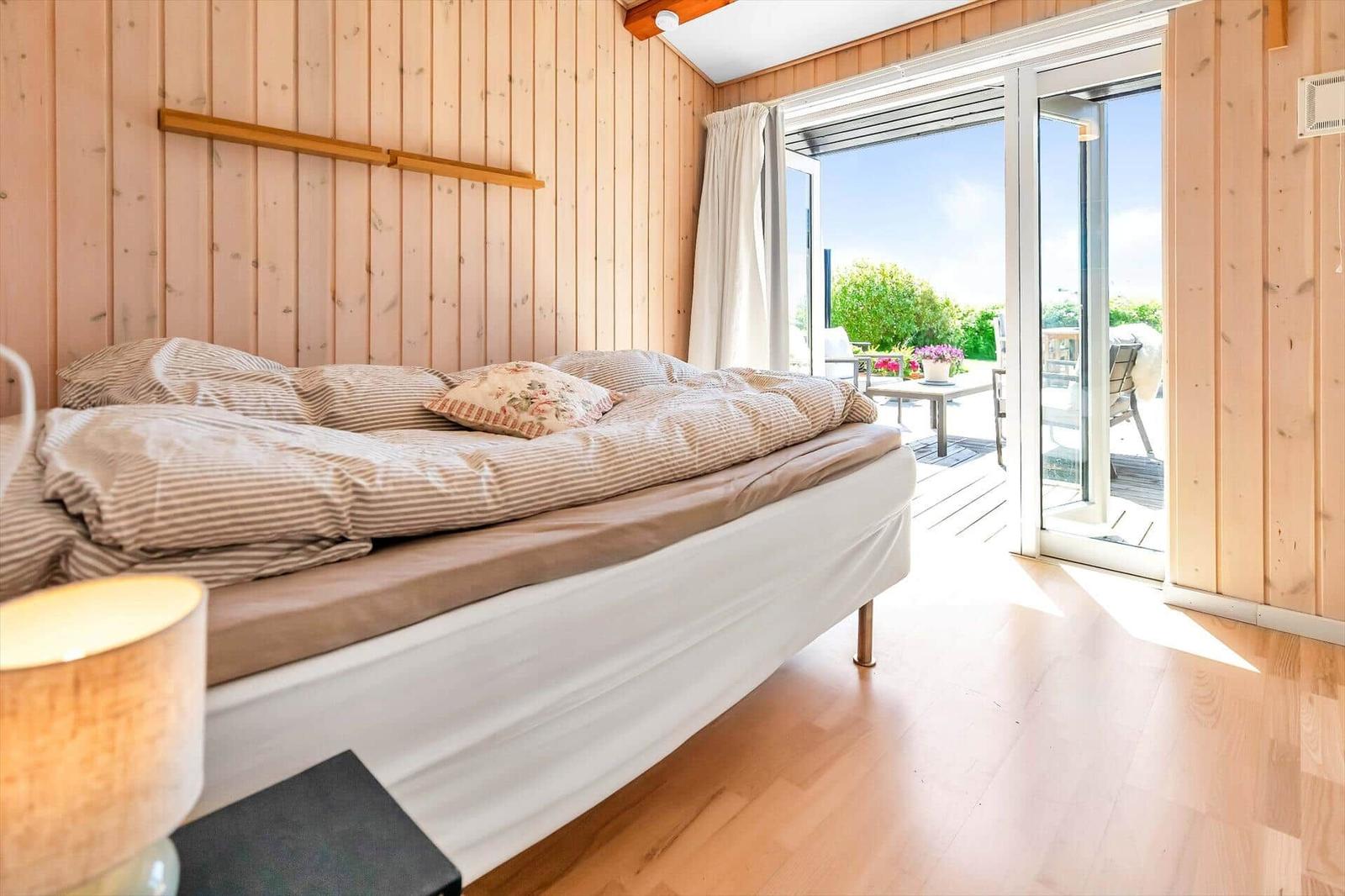 Schlafzimmer mit Bett, Holzwand und Glasschiebetür zum Balkon.