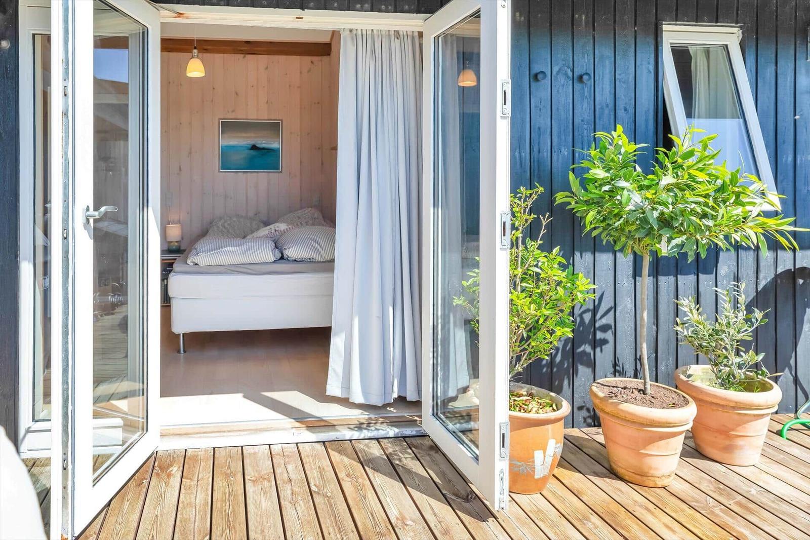 Durchgehende Glastür führt von der Terrasse ins Schlafzimmer mit Bett und Wandbild.