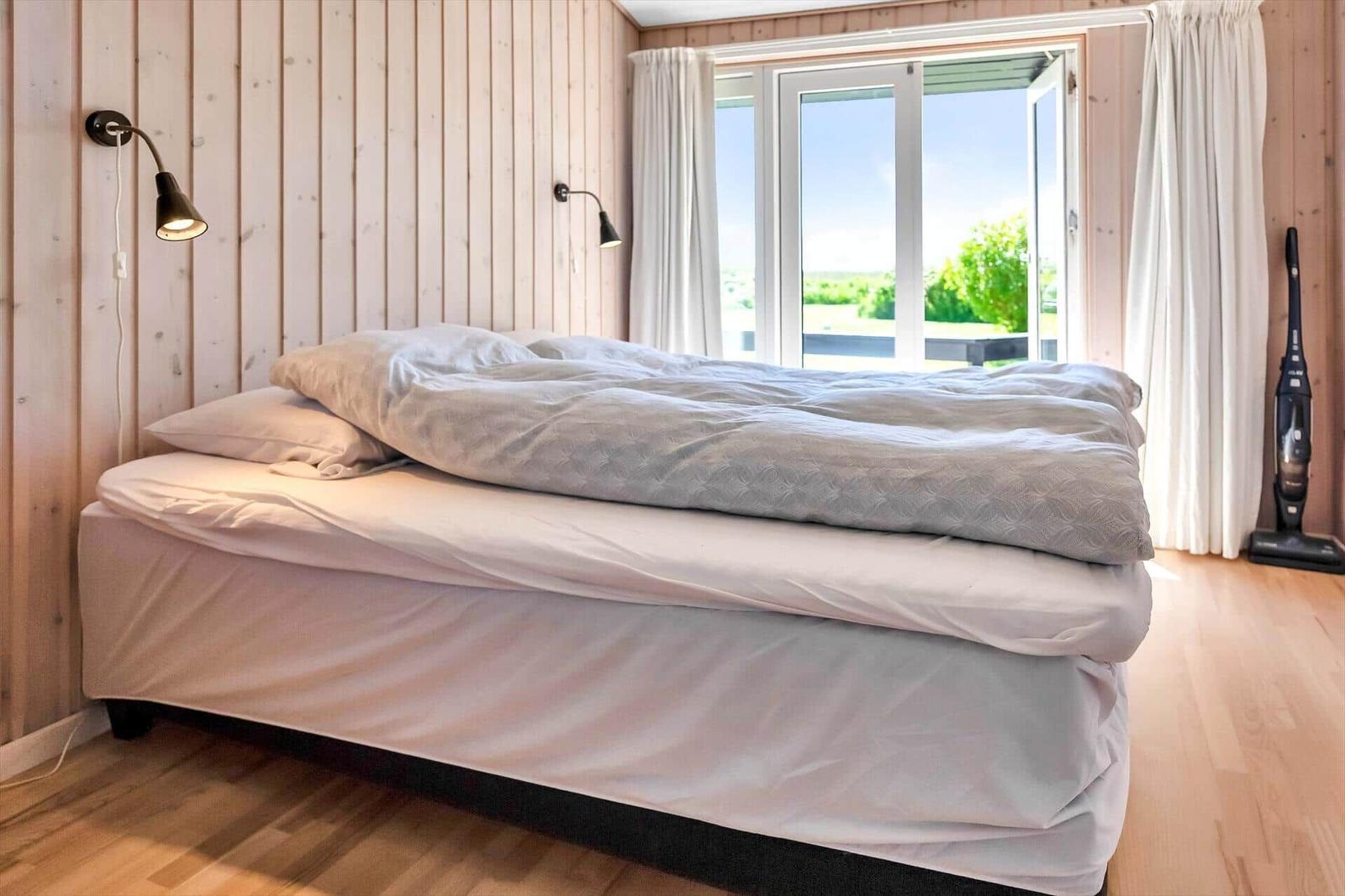 Schlafzimmer mit Bett, Holzwand und Fenster zur Terrasse