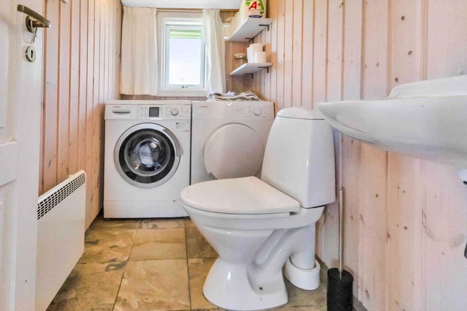 Badezimmer mit Toilette, Waschmaschine und Trockner, Holzwand und Fenster