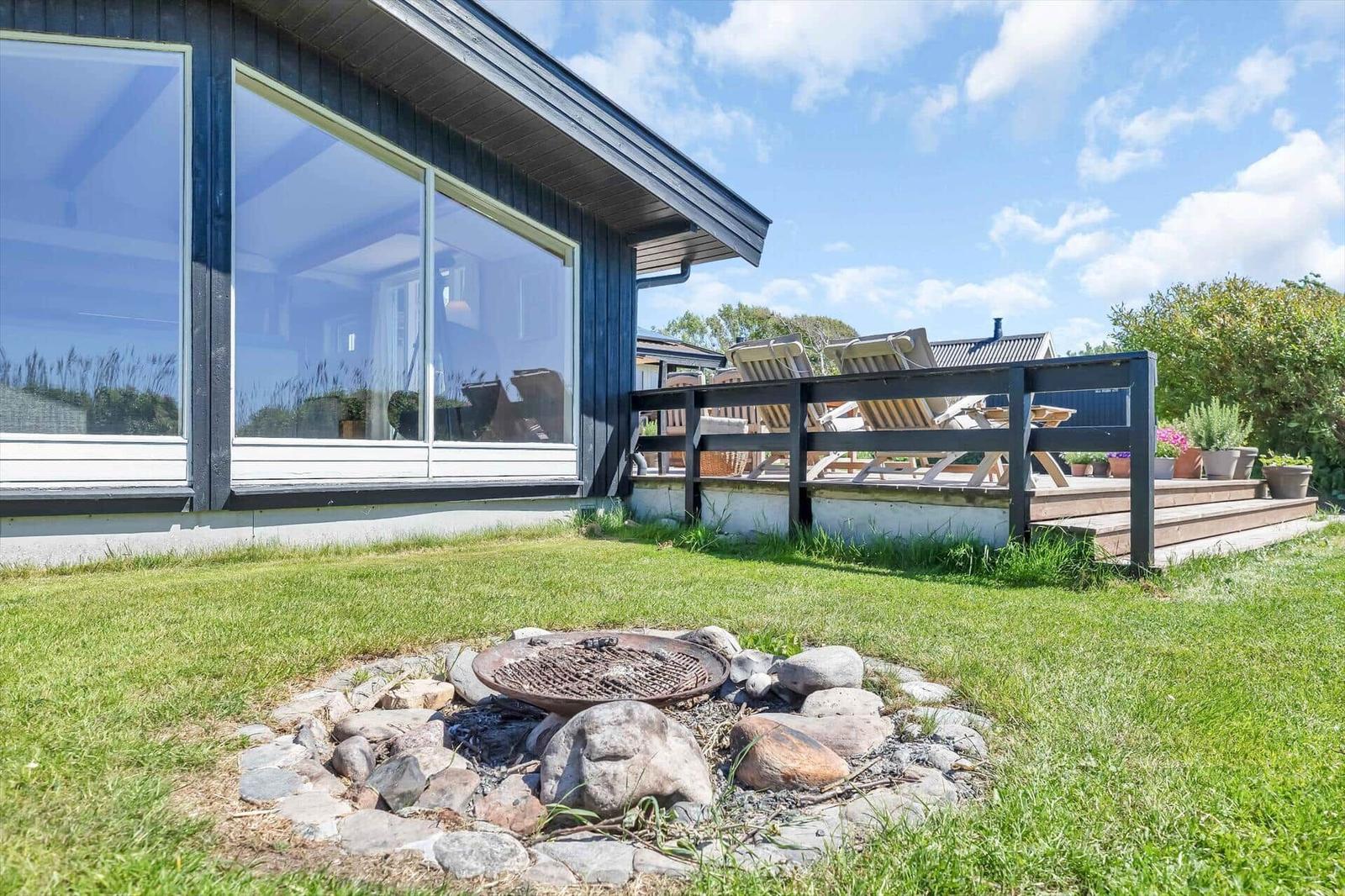 Haus mit Terrasse, Liegestühlen und Grillplatz im Garten.