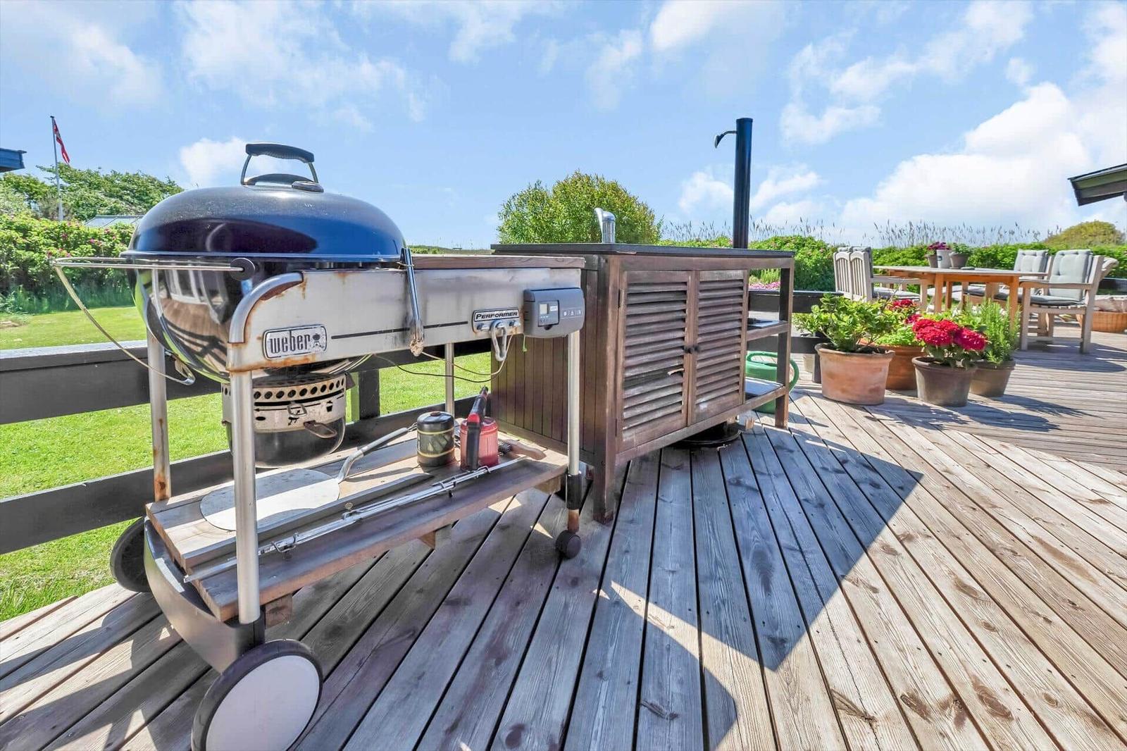 Terrasse mit Grill, Pflanzen und Sitzgelegenheiten.